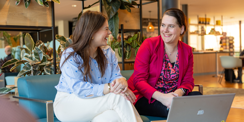 Sjanna en Mandy zitten op een blauwe bank en zijn met elkaar in gesprek.
