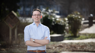 Collega André staat buiten het provinciehuis en kijkt glimlachend naar de camera.