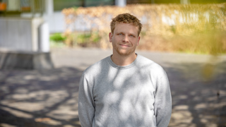Collega Koen staat buiten het provinciehuis en heeft een grijze trui aan.