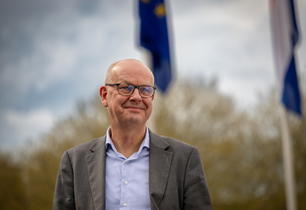 Sander staat buiten het provinciehuis onder de Europese vlag en Floor leunt tegen een reling in de natuur.