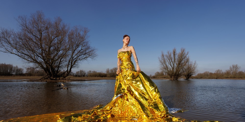 Vrouw in gouden jurk staat buiten in water.