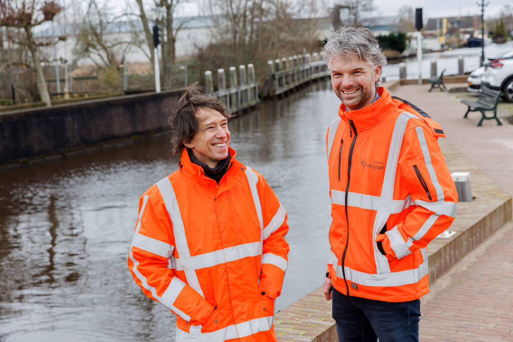 Een foto van collega's Bart en Johan die bij de kade in Ossenzijl staan met een oranje jas van de provincie aan.