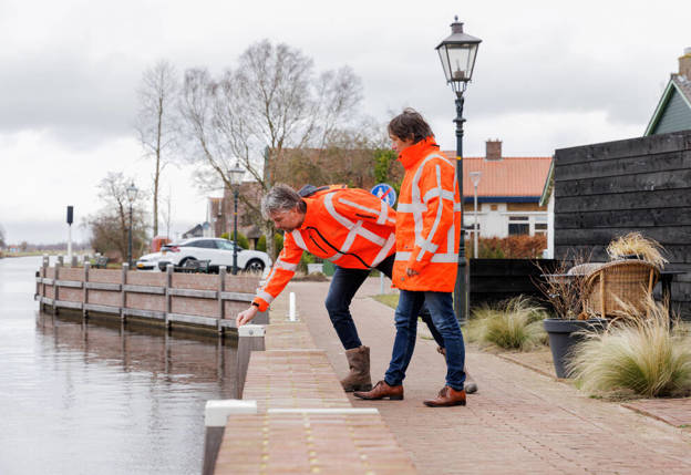 Op de eerste afbeelding is een kade in Ossenzijl te zien en op de tweede afbeelding staat diezelfde kade op de foto met collega's Johan en Bart erbij. Collega Johan wijst naar het water en is wat door zijn knieën.