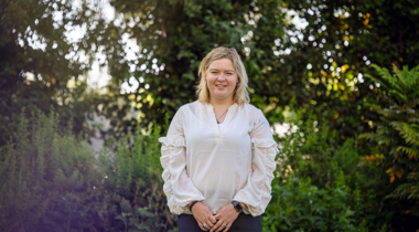Collega Lizet staat in de tuin bij het provinciehuis in Zwolle. Ze draagt een witte blouse en een zwarte broek. 