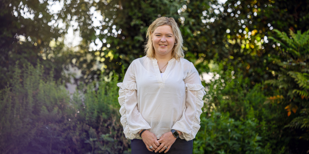Collega Lizet staat in de tuin bij het provinciehuis in Zwolle. Ze draagt een witte blouse en een zwarte broek.