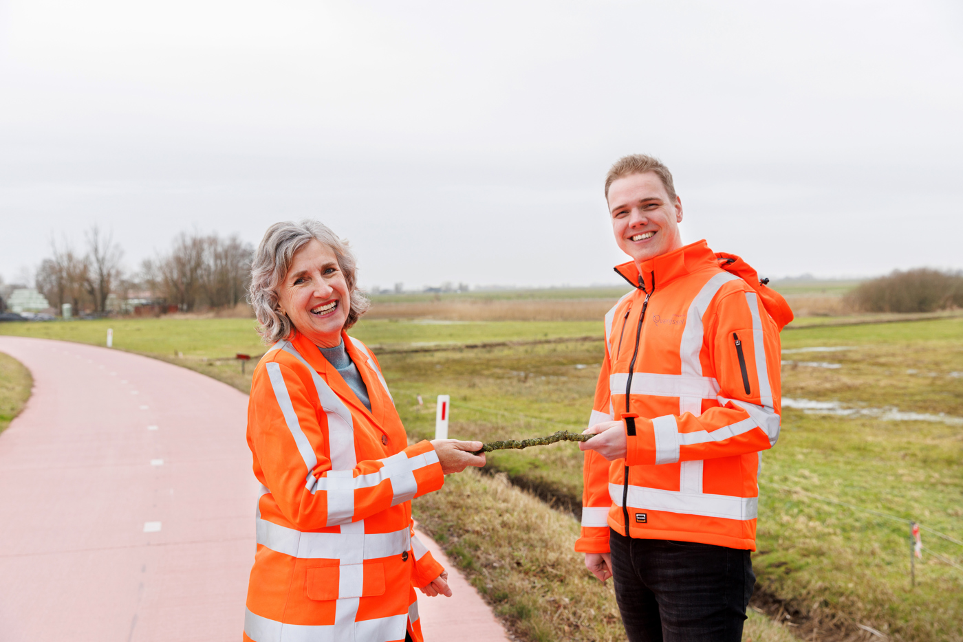 Op de afbeelding zijn collega's Eiberlien en Tiemen te zien. Eiberlien geeft hier letterlijk een stokje aan collega Tiemen.