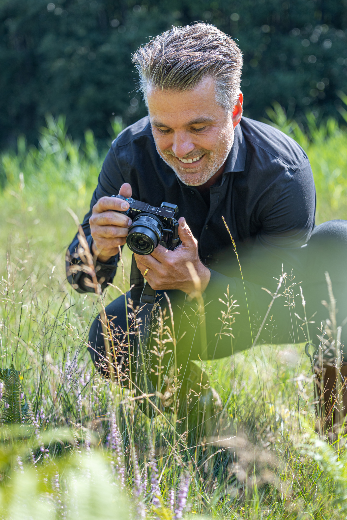 Collega Ives zit gehurkt tussen het gras en houdt een camera vast waar hij naar kijkt.