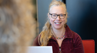 Collega Marjan zit achter een laptop. Ze draagt een rood pak.