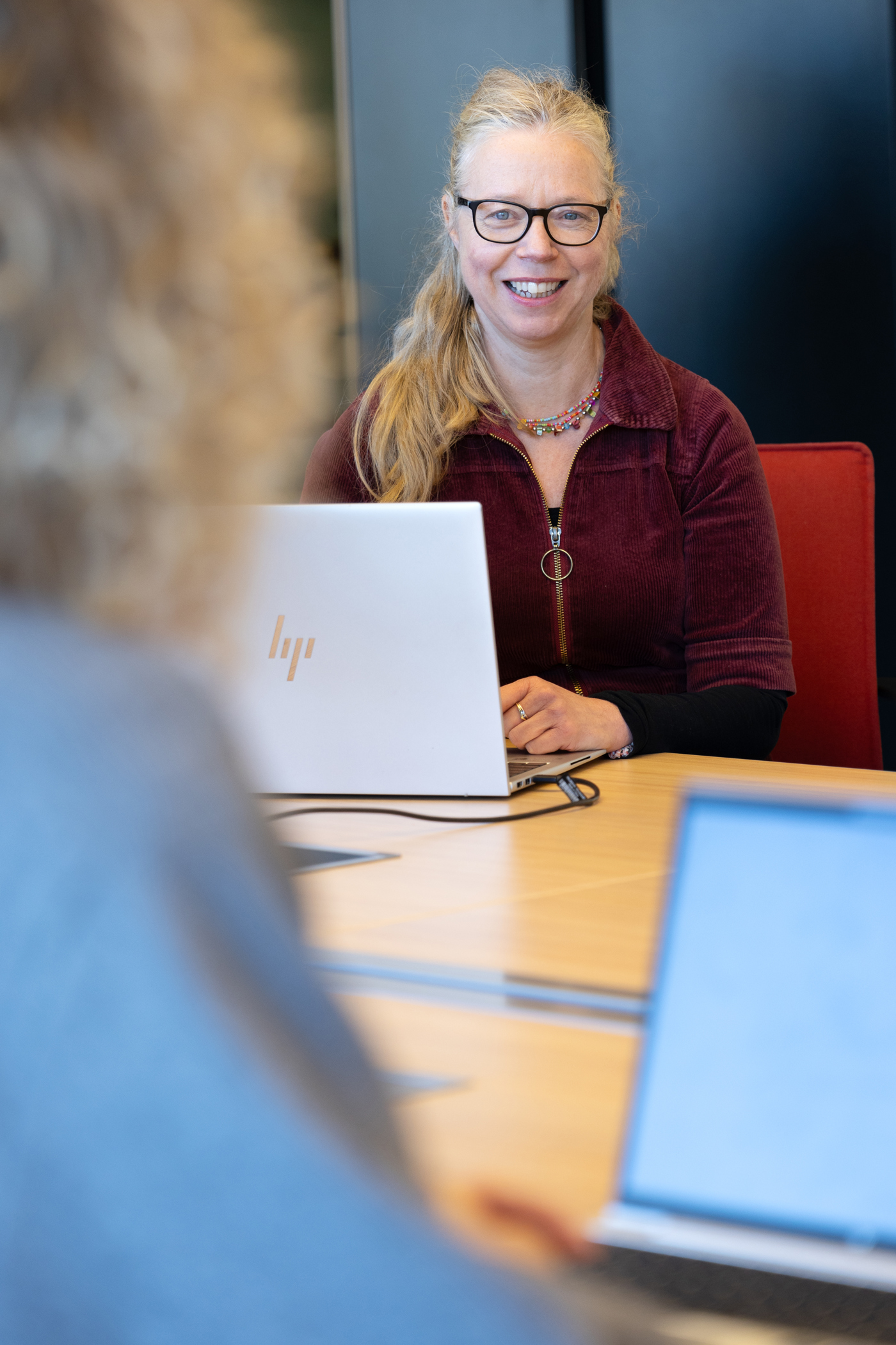 Collega Marjan zit achter een laptop. Ze draagt een rood pak.