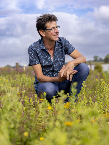 Collega Chris zit gehurkt tussen de natuur in het Vreugderijkerwaard op de eerste afbeelding. Collega Chris kijkt door een verrekijker bij het Vreugderijkerwaard op de tweede afbeelding.