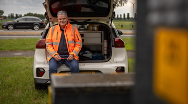 Collega Gerdjan draagt een oranje hesje en zit in de achterbank van een auto.