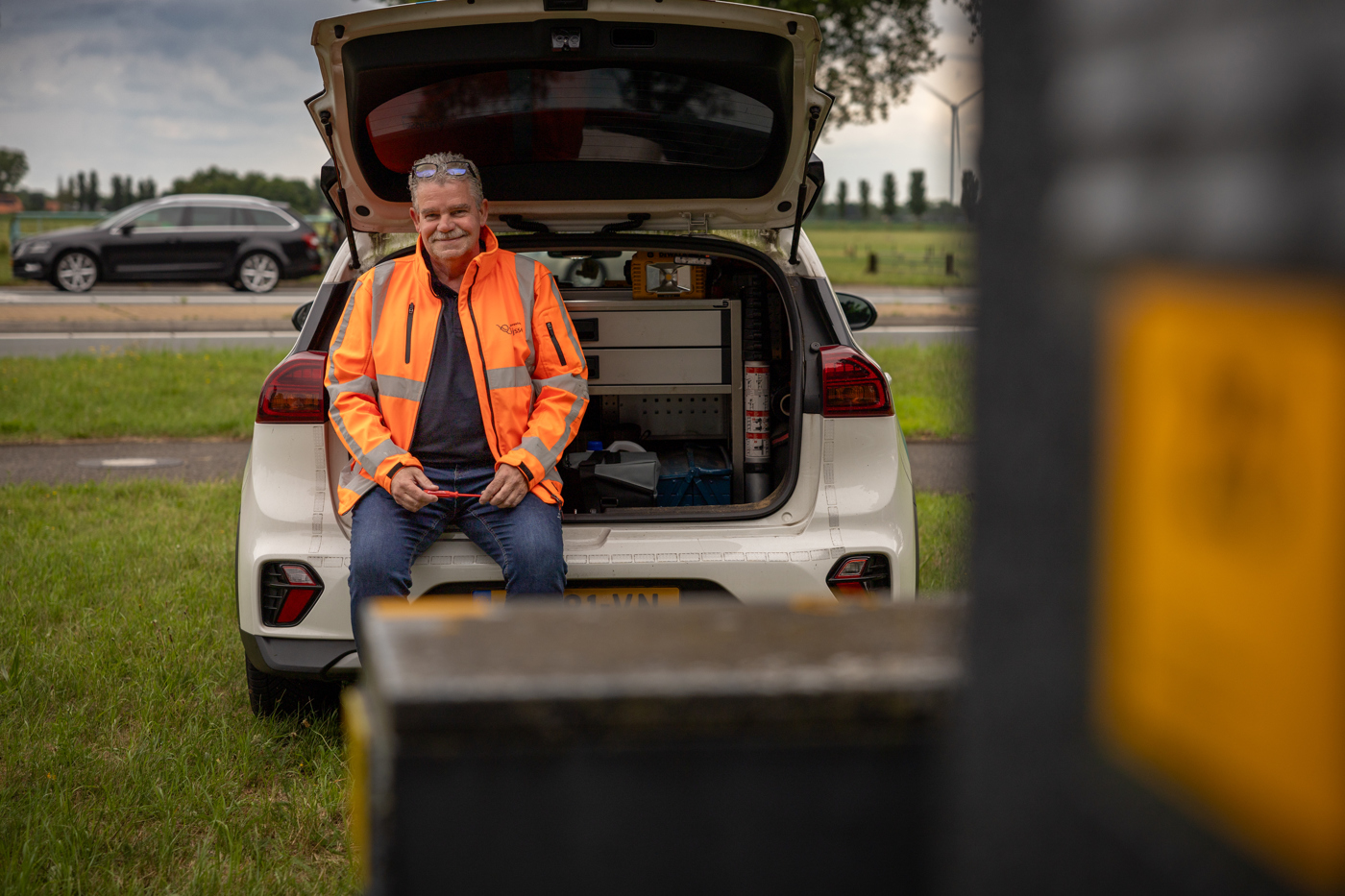 Collega Gerdjan draagt een oranje hesje en zit in de achterbank van een auto.