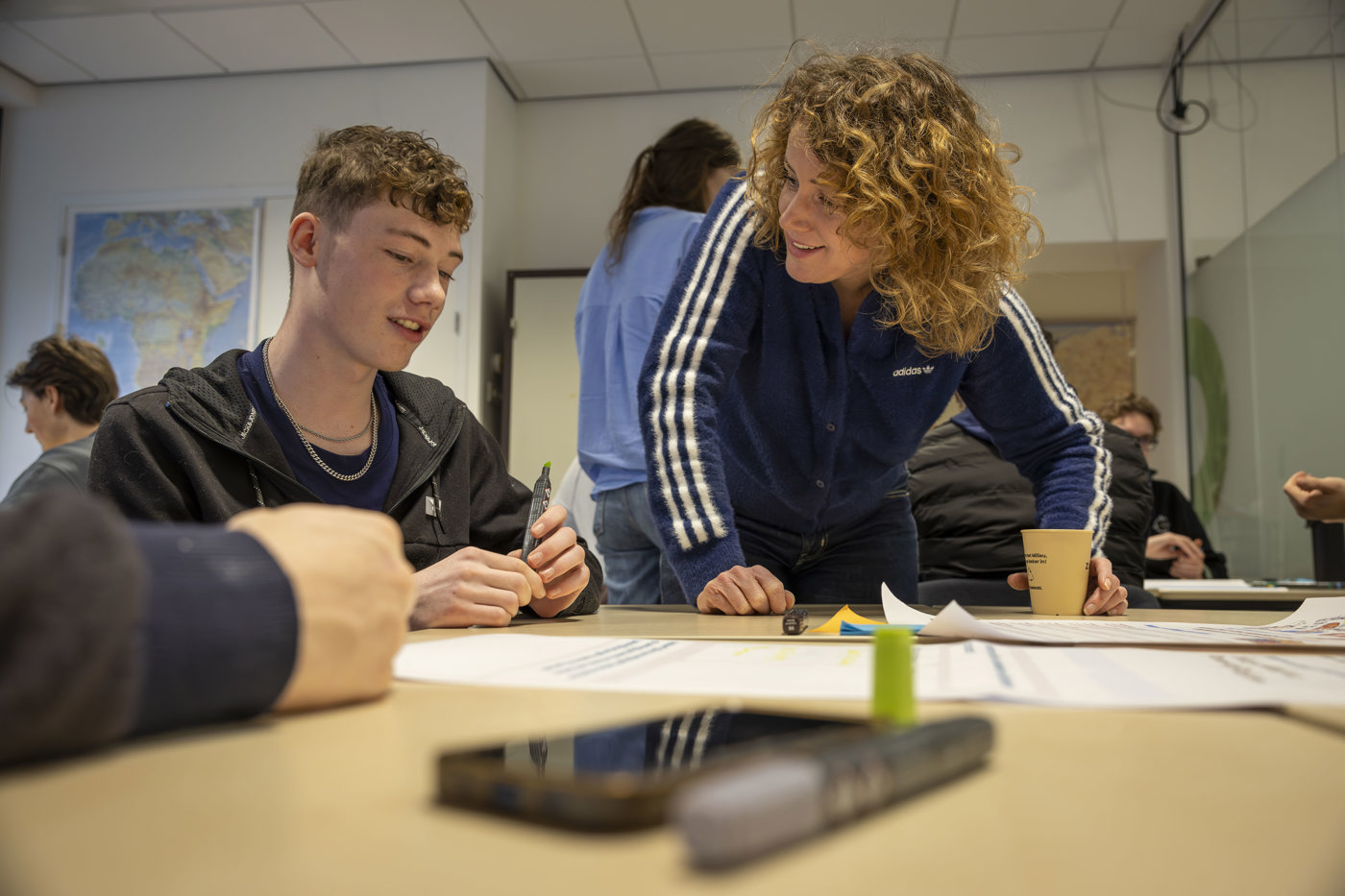 Collega Manon staat bij een tafel en is in gesprek met jongeren.