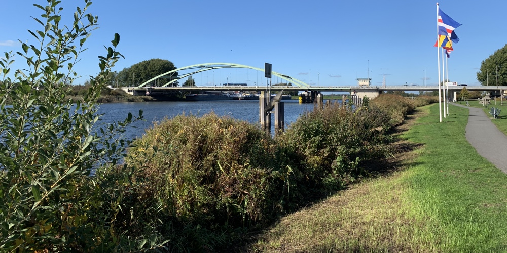 Zwartewaterbrug over het water, 3 vlaggen aan de rechterkant, struiken en een fietspad