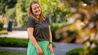 Collega Laura staat in de tuin bij het provinciehuis. Ze draagt een groene rok met witte bloemen en een grijs shirt.