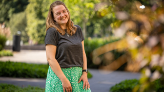 Collega Laura staat in de tuin bij het provinciehuis. Ze draagt een groene rok met witte bloemen en een grijs shirt.