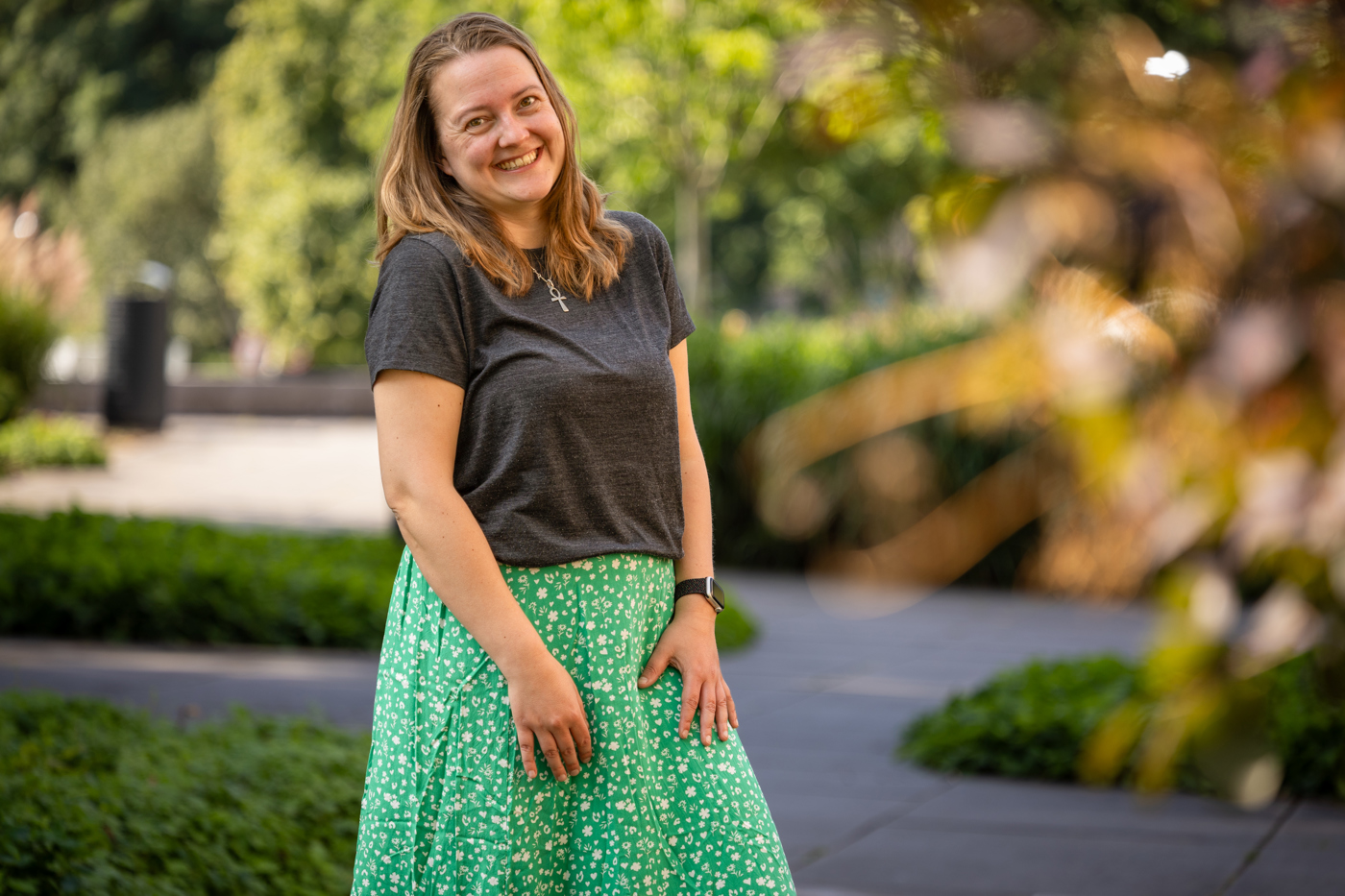 Collega Laura staat in de tuin bij het provinciehuis. Ze draagt een groene rok met witte bloemen en een grijs shirt.