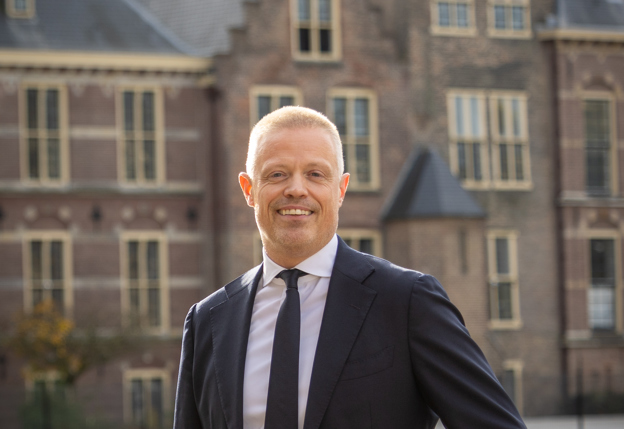 Collega Paul staat tegen een reling aan bij de Hofvijver in Den Haag. Hij draagt een donkerblauw pak.