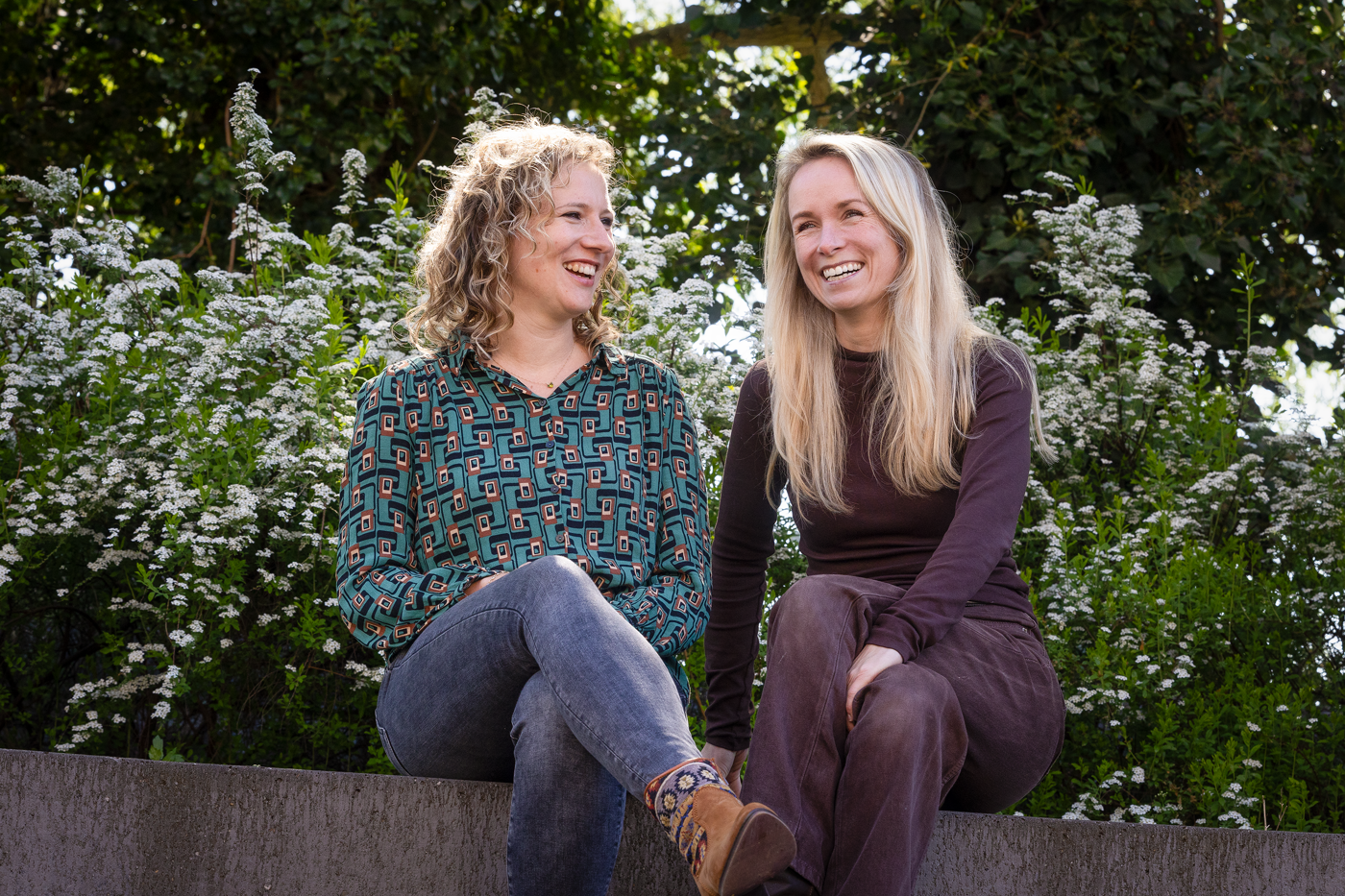 Collega's Nicole en Cynthia zitten glimlachend naast elkaar buiten op een bank.