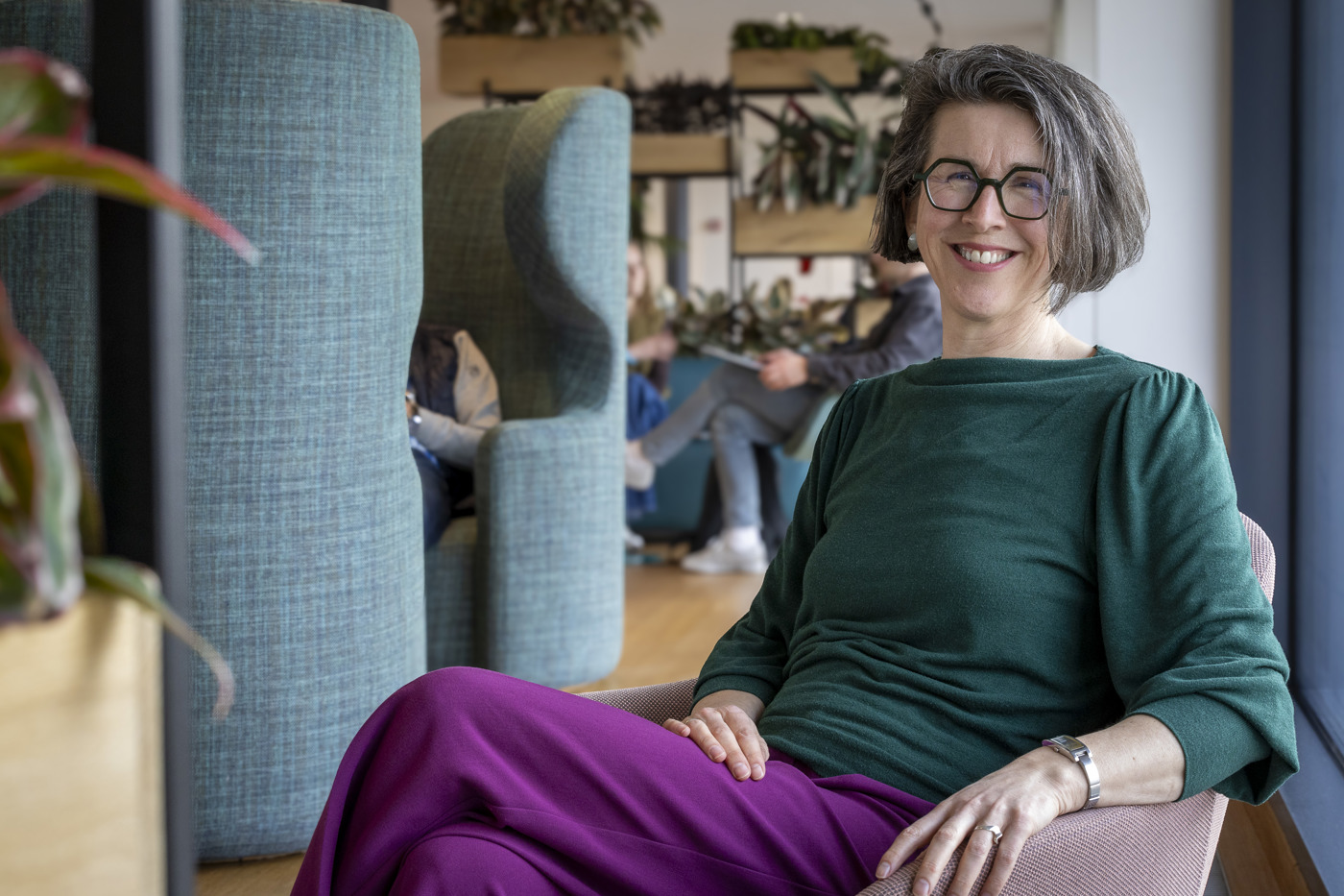 Annelies zit op een roze stoel en kijkt naar de camera