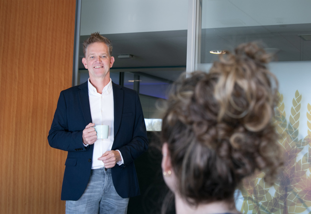 Op de eerste afbeelding is collega Jan Atze te zien waar hij op een bank zit terwijl hij belt. Op de tweede afbeelding is Jan Atze te zien terwijl hij in een deuropening staat met een kop koffie in zijn rechterhand. Hij is in gesprek met een dame wiens achterkant je op de voorgrond van de foto ziet.
