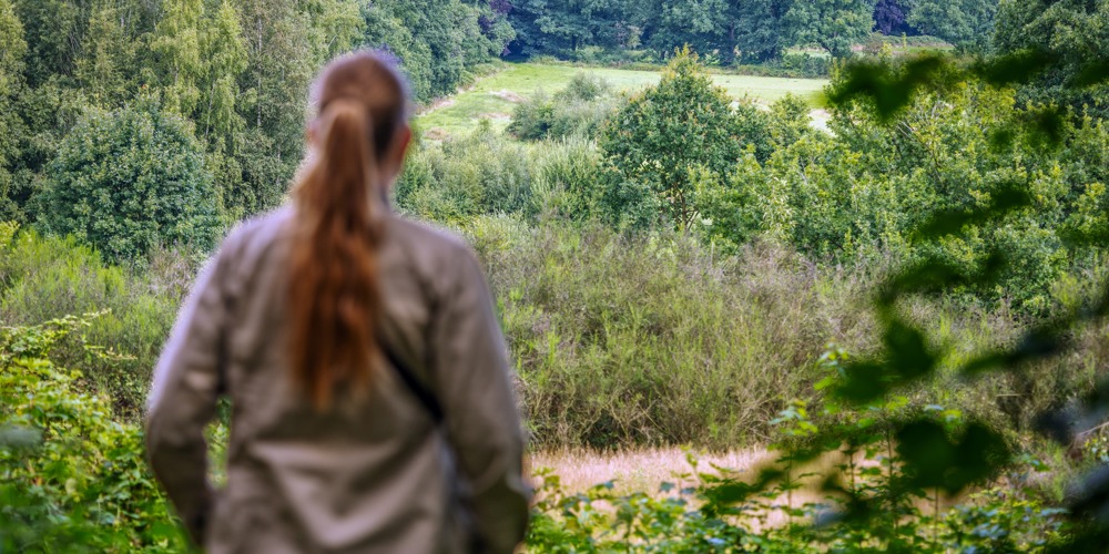 Collega Annemarie is van de achterkant vaag te zien en op de achtergrond is veel Overijssels natuur te zien met veel bomen.