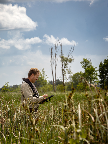 Collega Rinze staat in een natuur gebied in een veld met op de achtergrond wat bomen. Hij kijkt op een tablet.