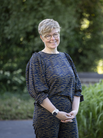 Op de eeste afbeelding zit collega Björn op een rode bank en achter hem is een plaat te zien met veel verschillende kleuren en de titel woonkeuken staat erop. Op de tweede afbeelding staat collega Marieke in de tuin buiten het provinciehuis. Er zijn bomen en grassen te zien op de achtergrond.