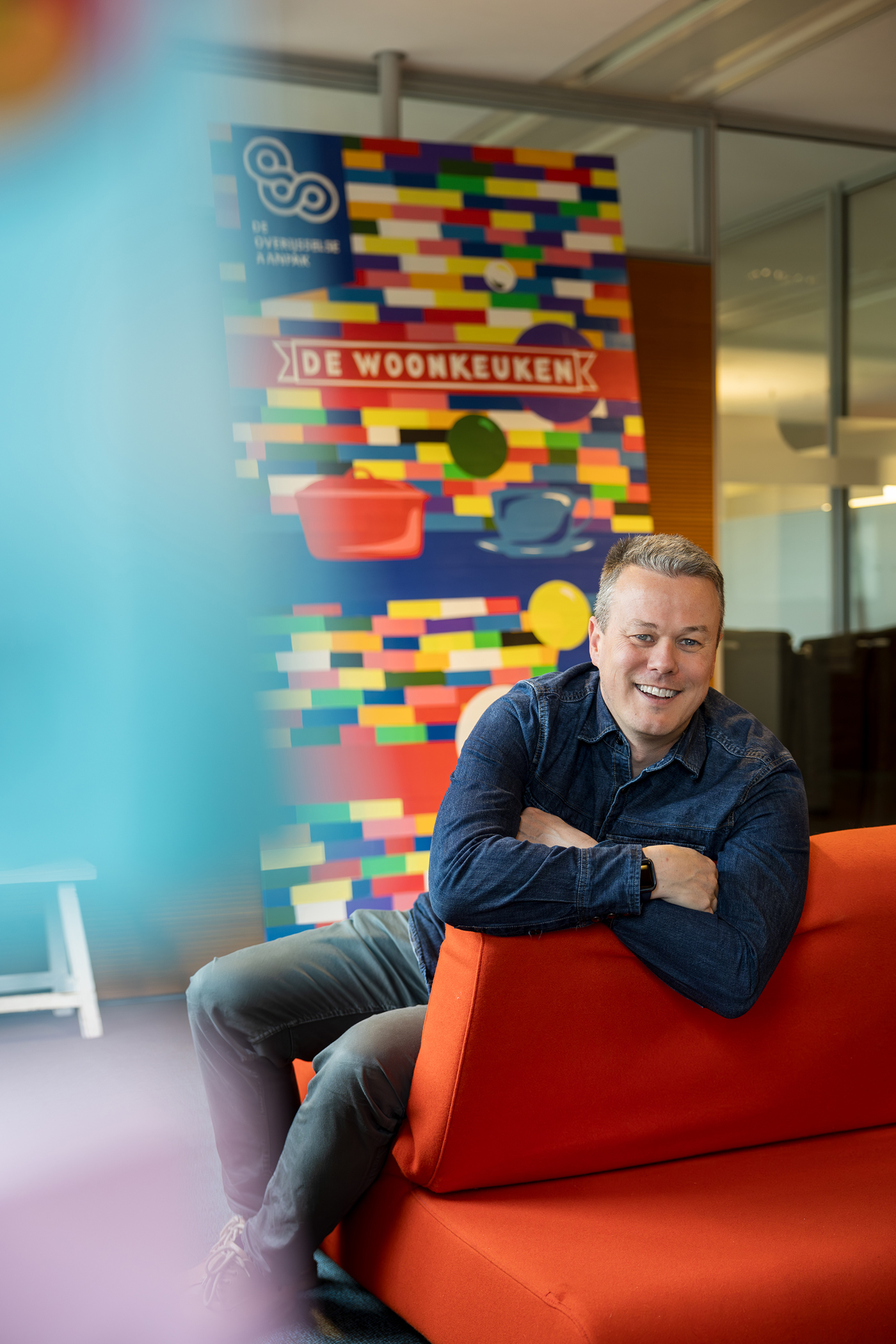 Een foto van collega Björn die op een rode bank zit. Achter hem is een poster te zien van de woonkeuken.