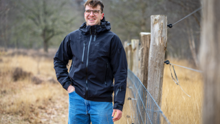 Collega Stijn staat in de natuur naast een hek en houten palen.