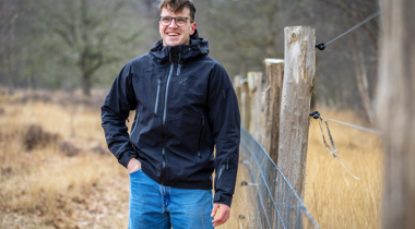Collega Stijn staat in de natuur naast een hek en houten palen.