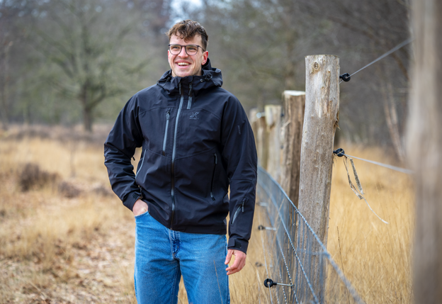 Collega Stijn staat in de natuur naast een hek en houten palen.